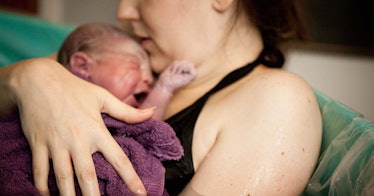 A mother holds a crying newborn in a home birth tub