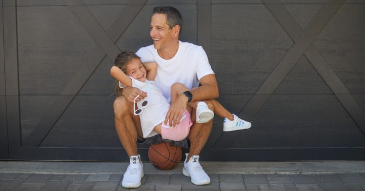 A father holds his daughter while sitting on a basketball
