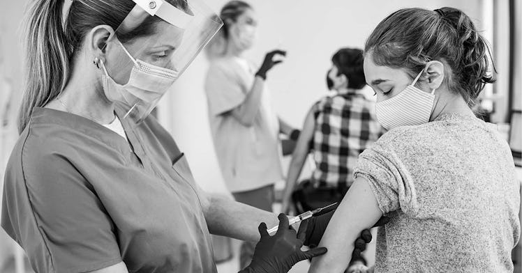 A tween gets vaccinated by a nurse in a face mask in black and white