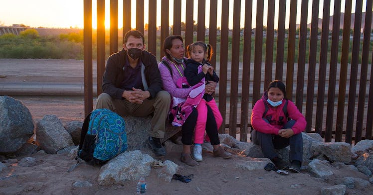 A migrant family sits at the border wall