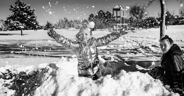 A kid in a puffer coat plays in the snow with their parent