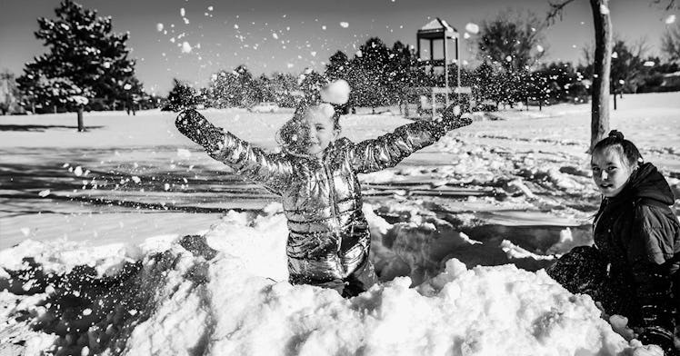 A kid in a puffer coat plays in the snow with their parent
