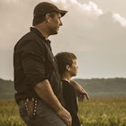 A father in a ballcap looks out at the horizon with his young son