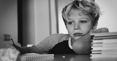 A boy leans up against stack of books looking sad