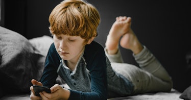 A young boy lays on the floor looking at a cellphone.