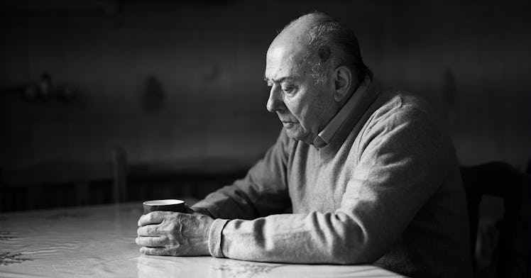 An old person sits at a table in black and white