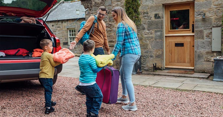 Parents and their two sons unpacking luggage from their car, in front of their Airbnb. 