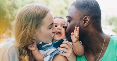 A white woman and a black man kiss a baby at the same time while the baby smiles
