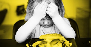 I child holds their head in their hands as they look at food they should be eating