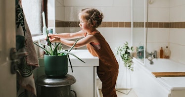A child washing his hands independently in a plant-filled bathroom
