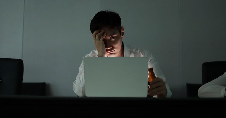A stressed out worker sits behind a laptop in the half-darkness