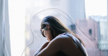A young Asian woman sits at a window looking pensive
