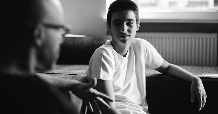 Black and white photo of a teen dad looking at his father while he talks
