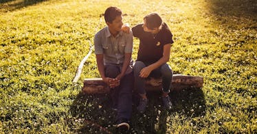 the boys sit on a log and one wraps his arm around the other