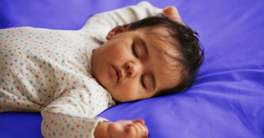 A baby sleeping against purple colored sheets.