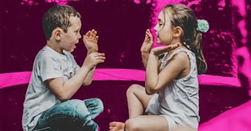Young boy and girl playing Pat-a-Cake in front of a pink background.