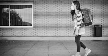 A kid walks down an outdoor hallway at a school, wearing a mask in black and white