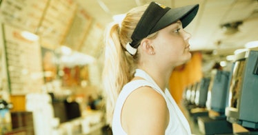 A white blond teenage girl in a visor stands in a fast food restaurant where she works