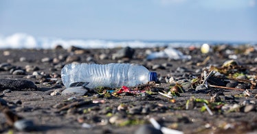 A beach with litter on it and an empty, crushed plastic bottle