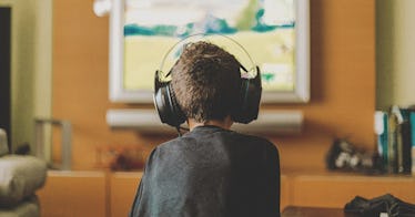 A kid faces away from the camera, playing video games with a headphone on