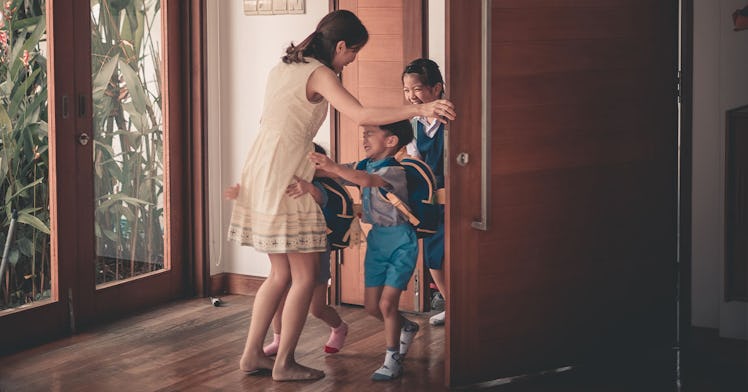 a woman hugs her kids as they walk in the door, back from school
