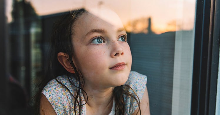 A kid sits inside, staring out a window