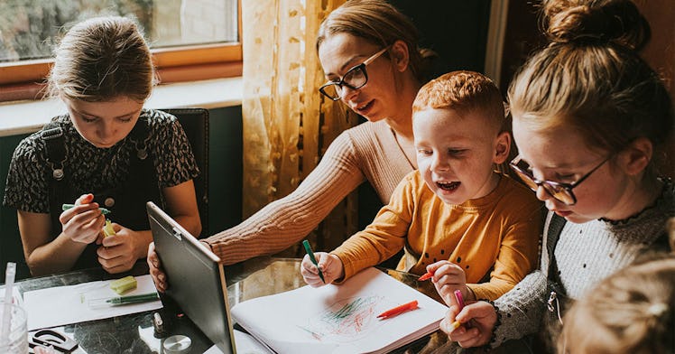 A mom, sitting at a table, has a kid on her lap and one on each side