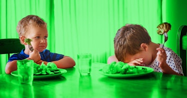 一个孩子在餐桌上吃着西兰花，另一个孩子在一旁看着