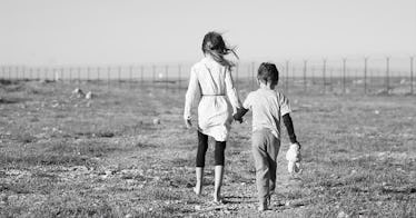 Two children walk away from the camera, in a field, in black and white