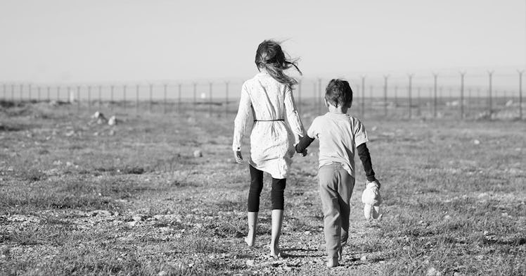 Two children walk away from the camera, in a field, in black and white