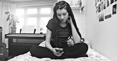 一个十几岁的女孩，穿着黑白相间的衣服，坐在床上