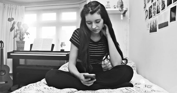 A teenage girl, in black and white, sits on a bed