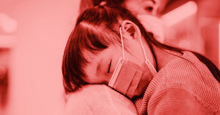 a child in a mask lays their head down on a parent's shoulder