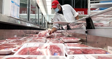 A grocery store worker stands over a fridge of meat