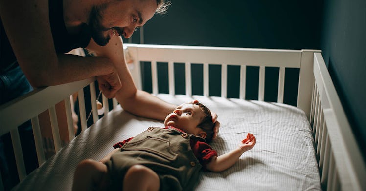 a father looks over at his sleeping daughter in a cot