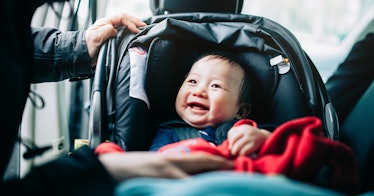 A baby smiles in a car seat