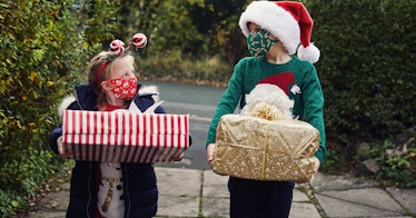 Two children, decked out in Christmas regalia, carrying presents, wearing masks