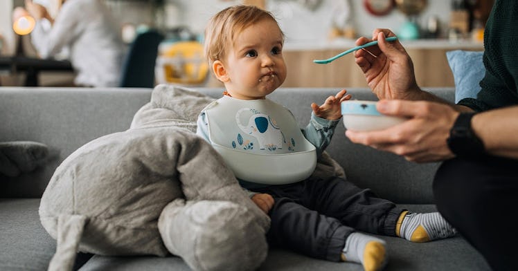 A parent feeds a baby a spoonful of Cheerios from a bowl.