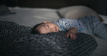 A baby wearing blue pajamas sleeping on a bed