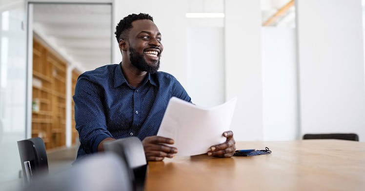 a guy at a desk holds a paper in his hands and smiles