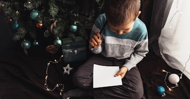 A kid sits at his Christmas tree with a letter