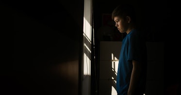 一个孩子悲伤地站在黑暗的房间里。