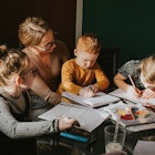 A woman sitting with children while they're drawing on papers