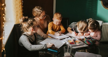 A woman sitting with children while they're drawing on papers