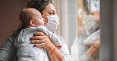 A mom wearing a mask holds a baby.