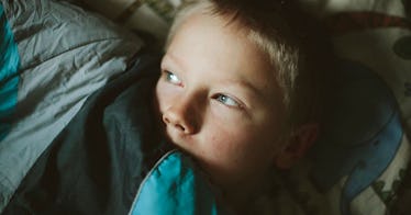 A scared child hiding his face under blankets due to ineffective parenting style habits that make ki...