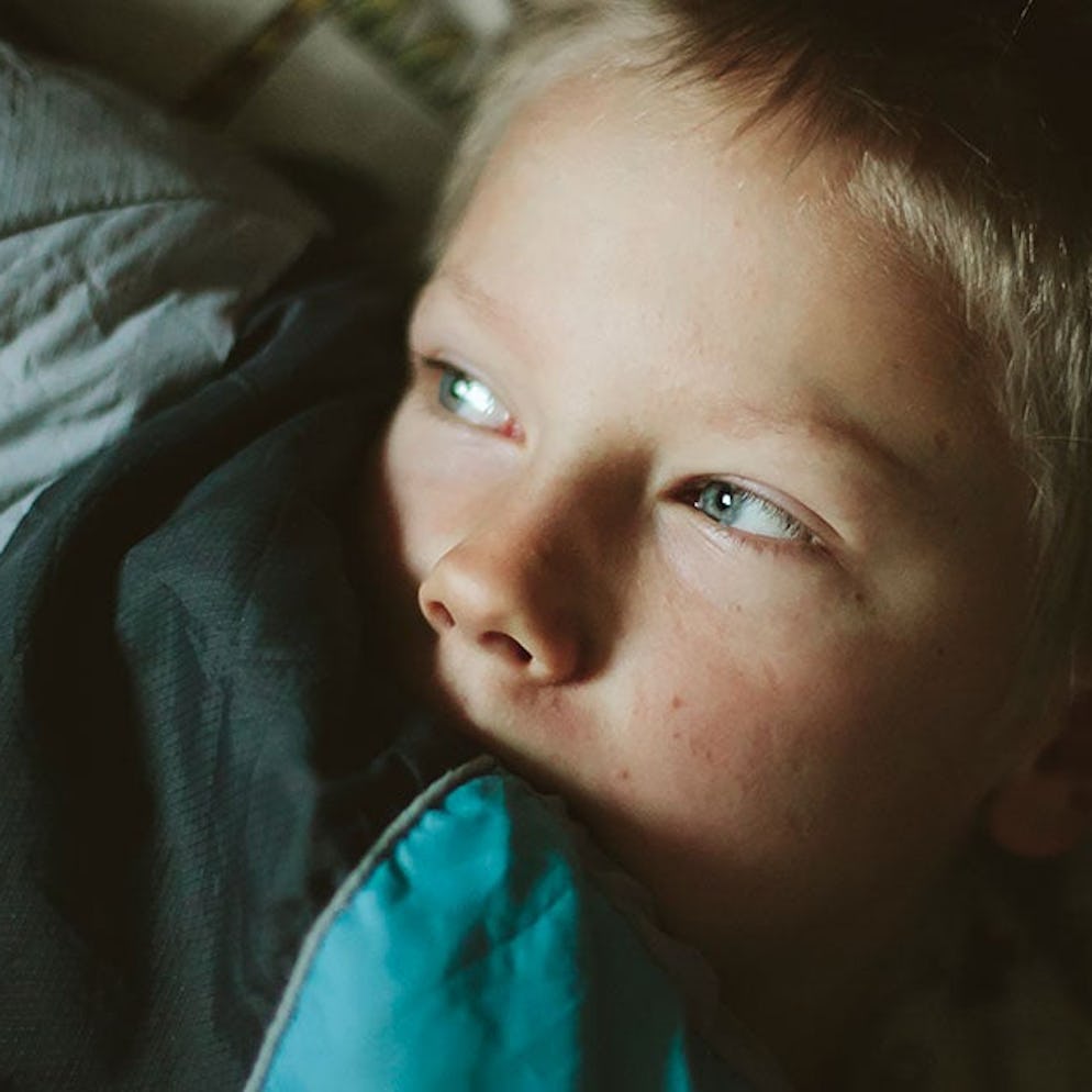 A scared child hiding his face under blankets due to ineffective parenting style habits that make ki...