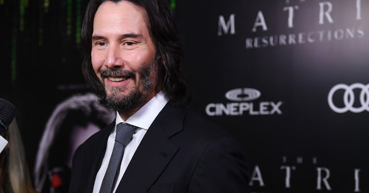 Keanu Reeves smiling and posing in a black suit, white shirt and a black tie at the Matrix movie pre...