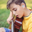 a child wearing a hearing aid strums a guitar