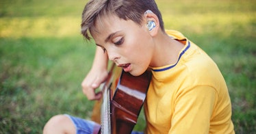 a child wearing a hearing aid strums a guitar